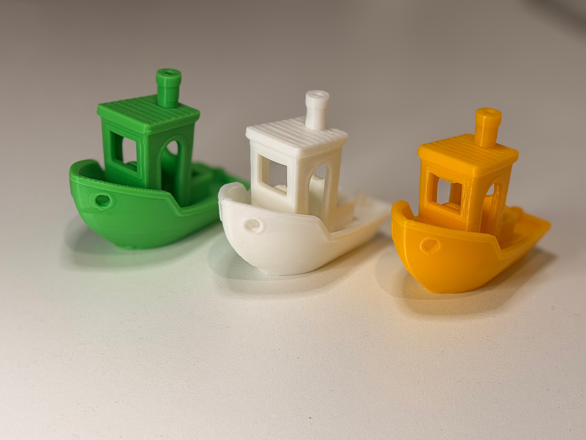 Three small 3D-printed boats in bright green, white and golden yellow, with their printed layers visible.